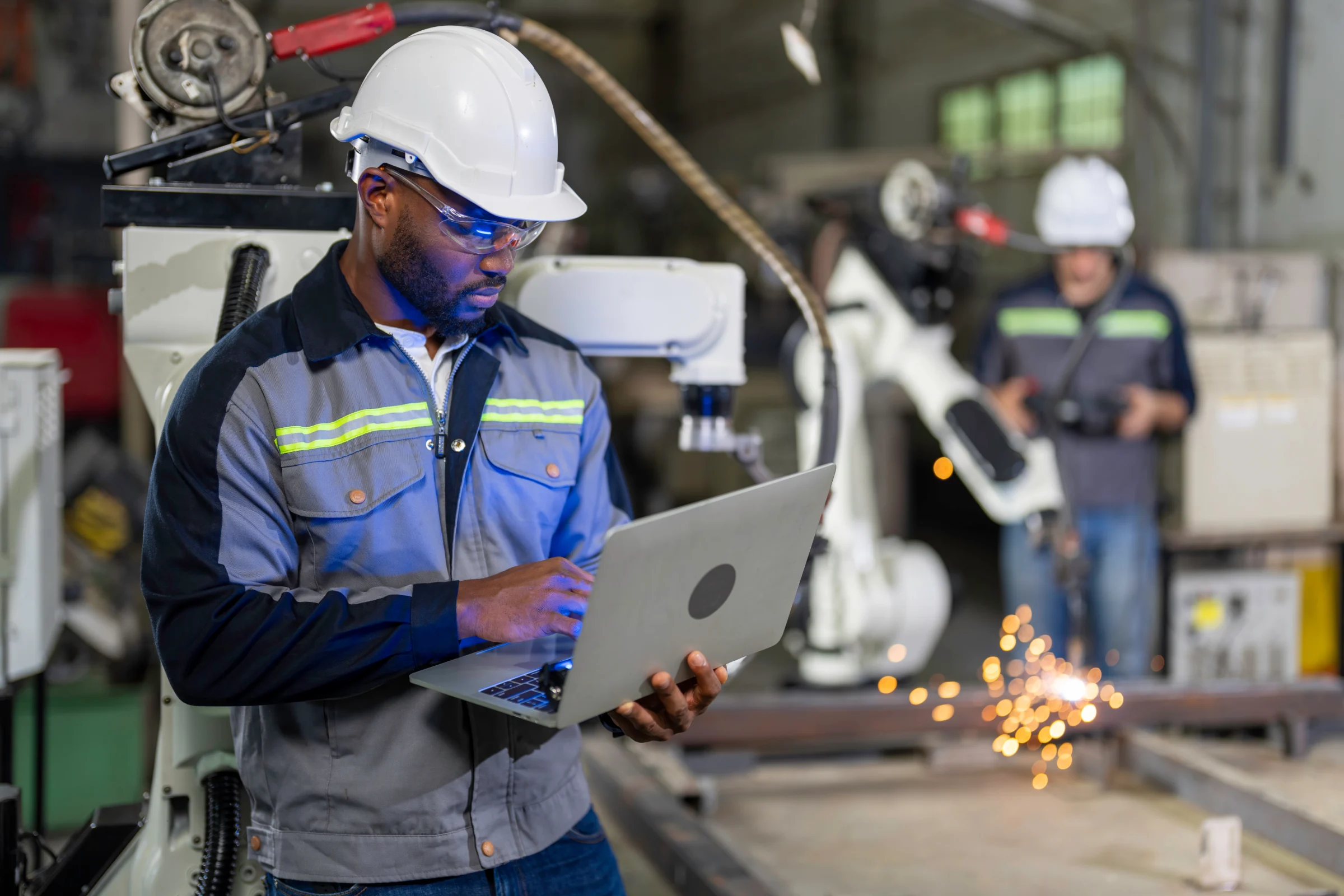 Manufacturing technician using a laptop beside production machinery.