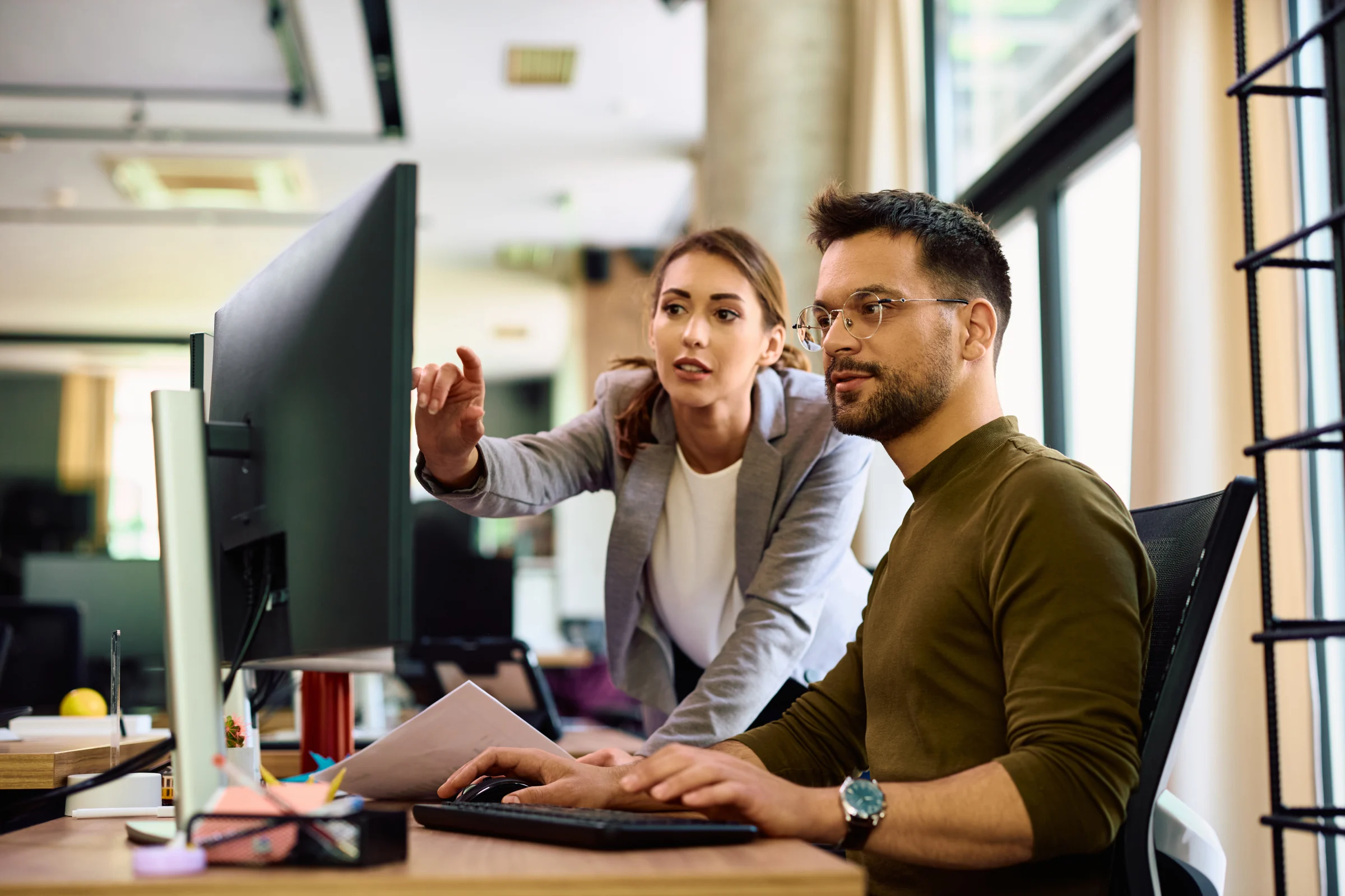 Colleagues reviewing work together at a desktop computer.